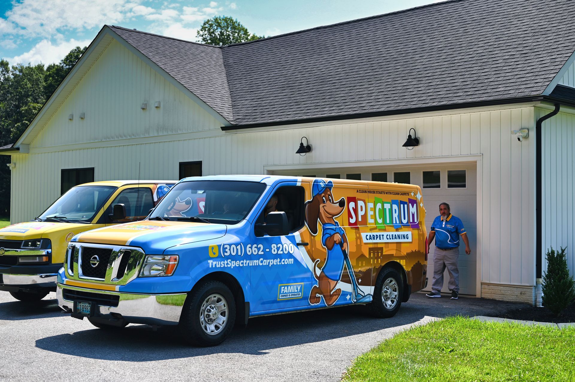 Two Spectrum service vans parked in front of a white building with a man standing by one van.