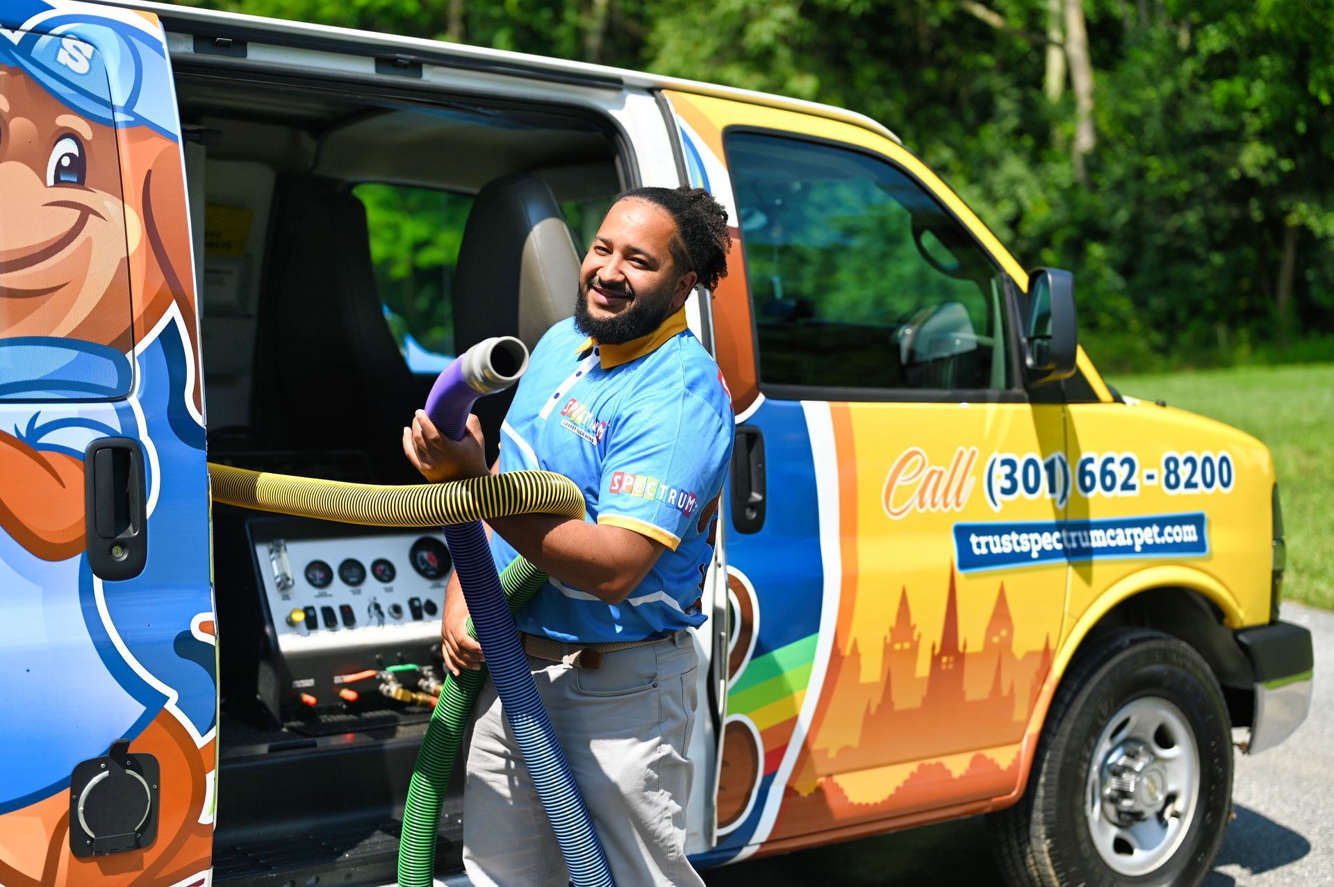 Man holding hose beside a yellow service van with a cartoon mascot. He is smiling outside.