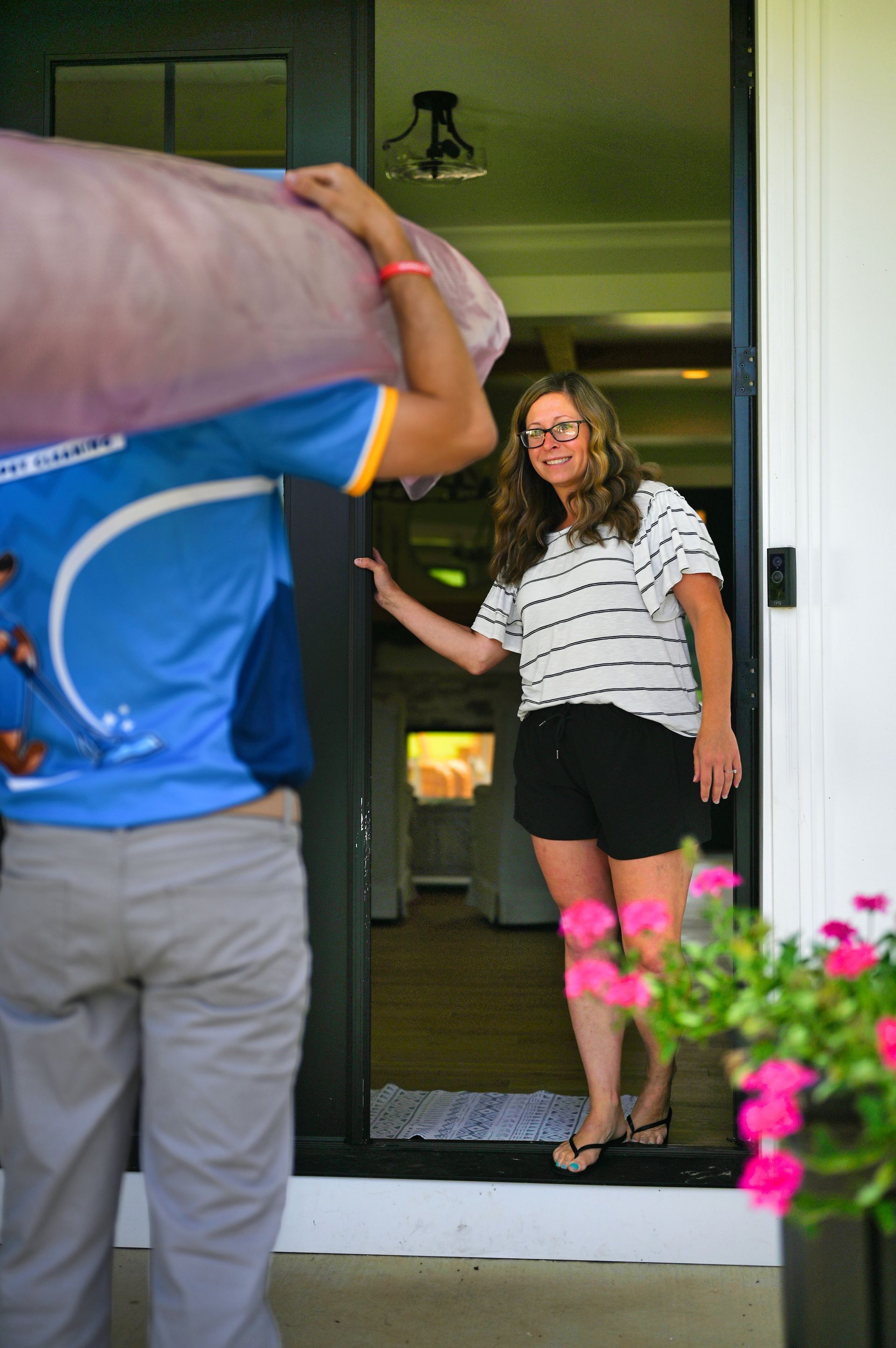 Woman greets a delivery person carrying a large rolled-up item, standing in her doorway.