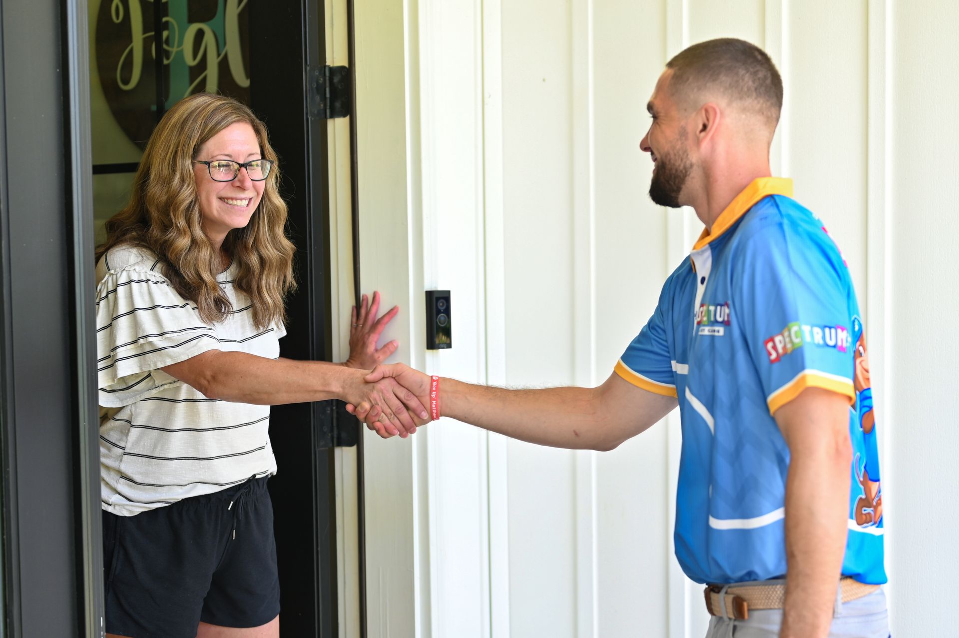 Woman shakes hands with a man in a doorway; both smiling, the man wearing a blue uniform.