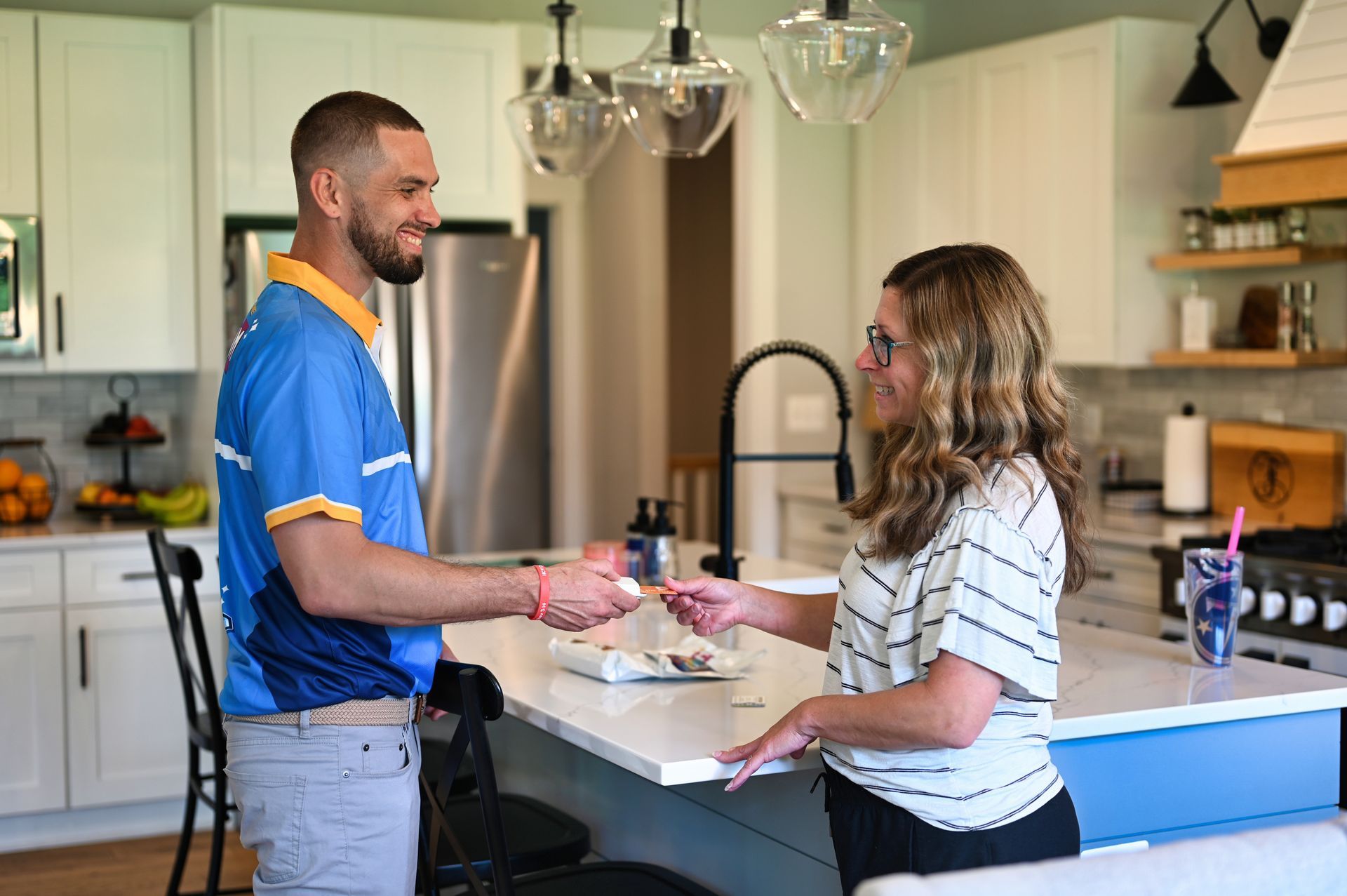Man in blue shirt handing food to woman in a modern kitchen.