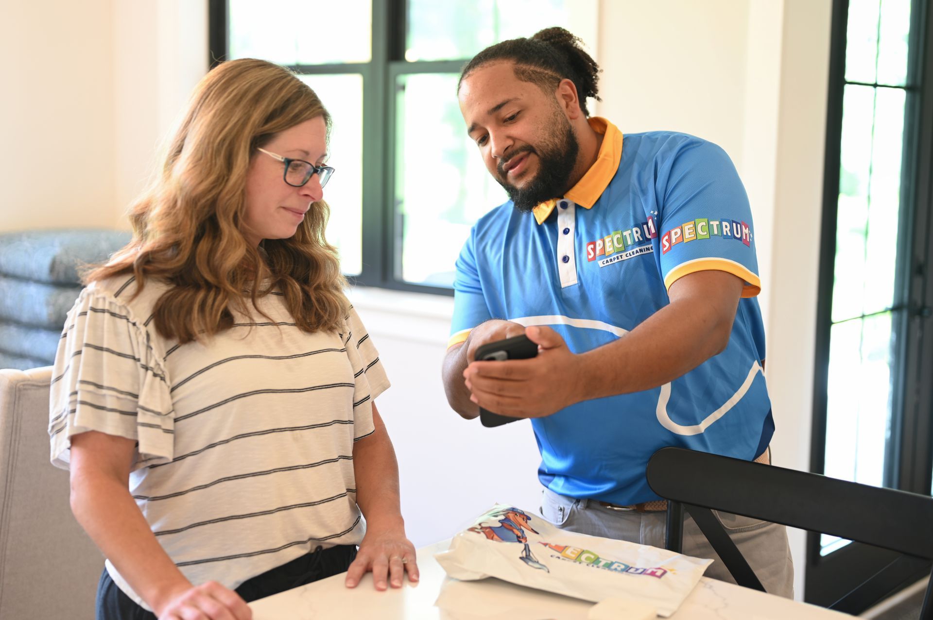 Woman and man looking at a phone. Man in blue uniform points to the phone, inside a house.