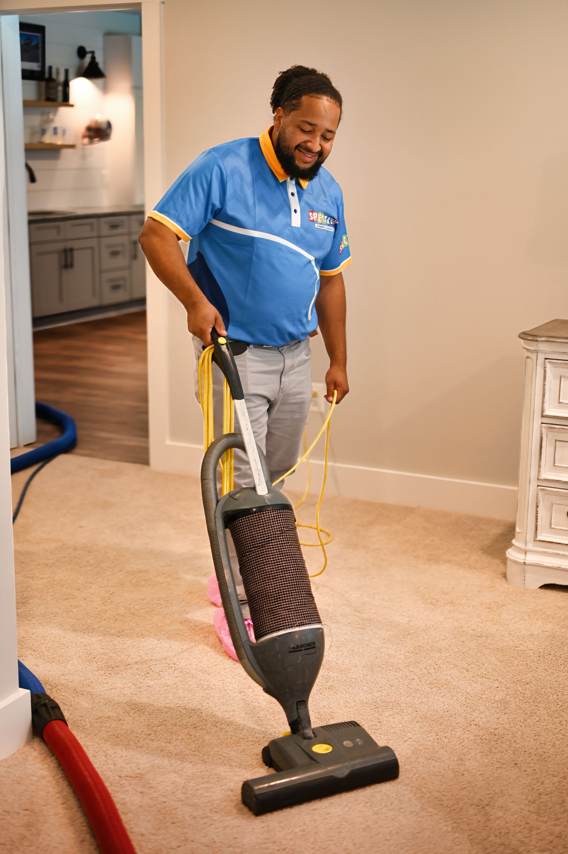 Man in blue shirt vacuums carpet in a room. He smiles.