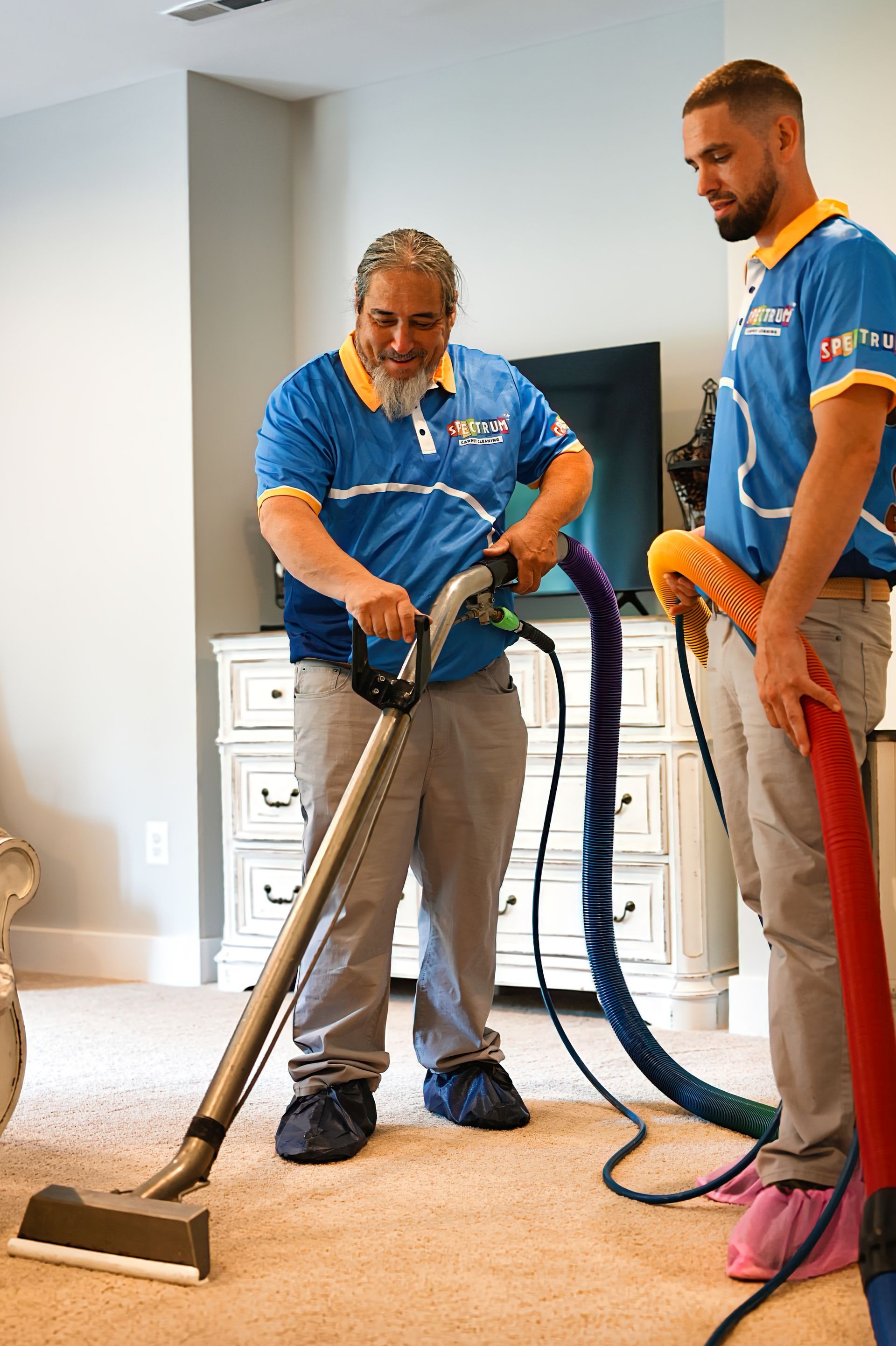 Two men cleaning carpet with industrial vacuum in a home. One operates the machine, the other holds a hose.