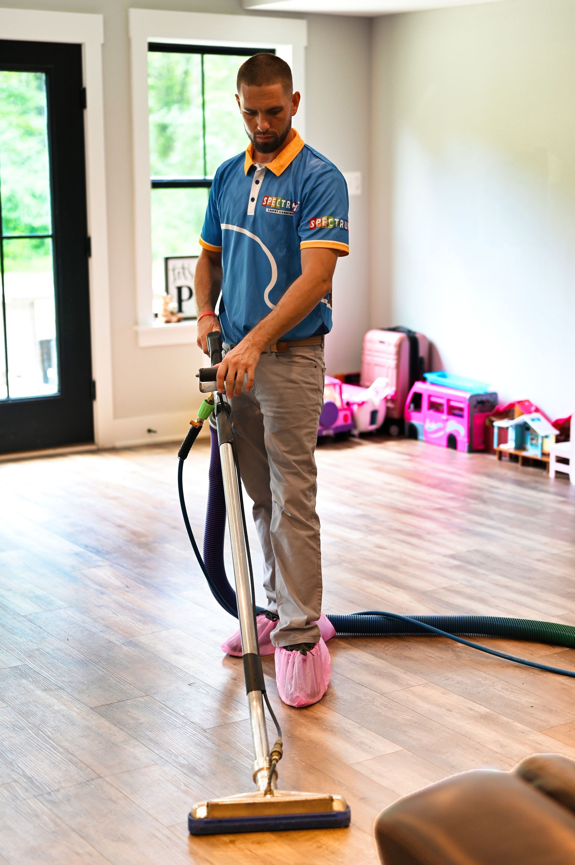 Man cleaning a floor with a machine, wearing pink shoe covers. Interior shot.