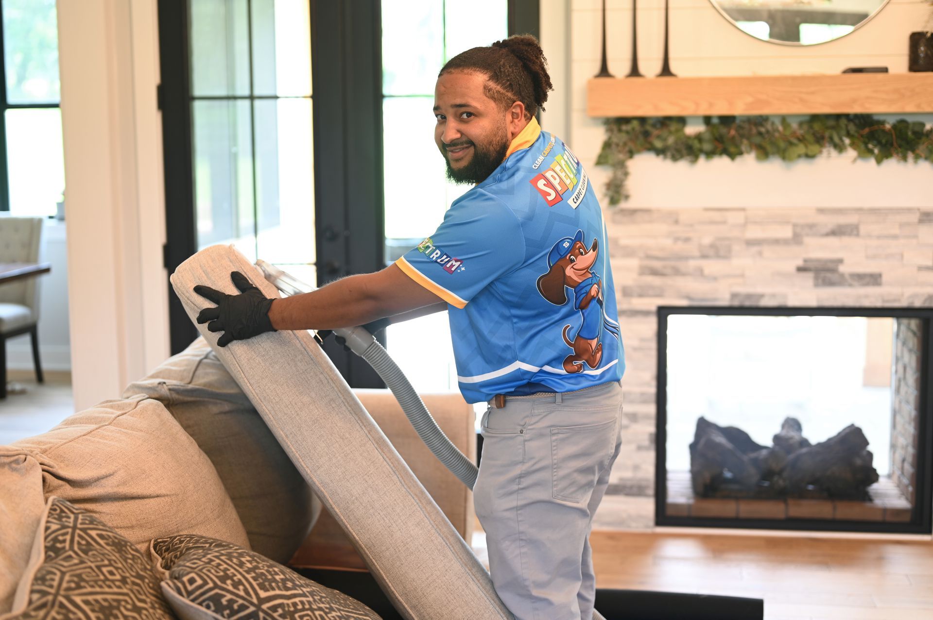 Man rolling up a rug on a sofa in a living room with a fireplace and a decorative mantel.