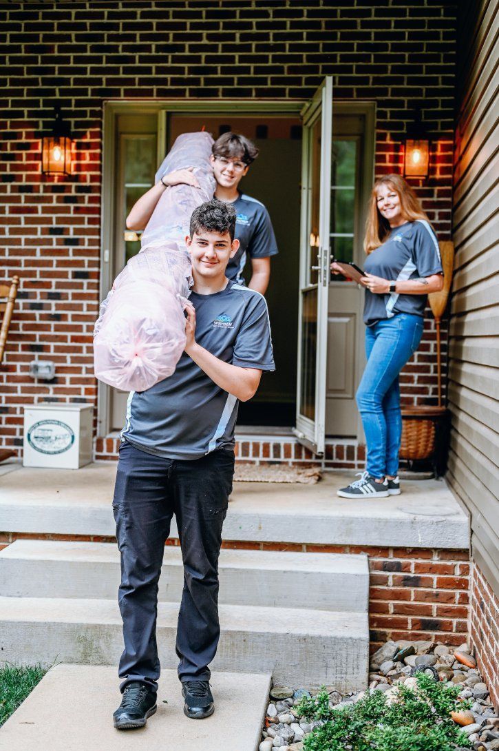 Three people unloading a large, wrapped item from a house, one carrying it on his shoulder.