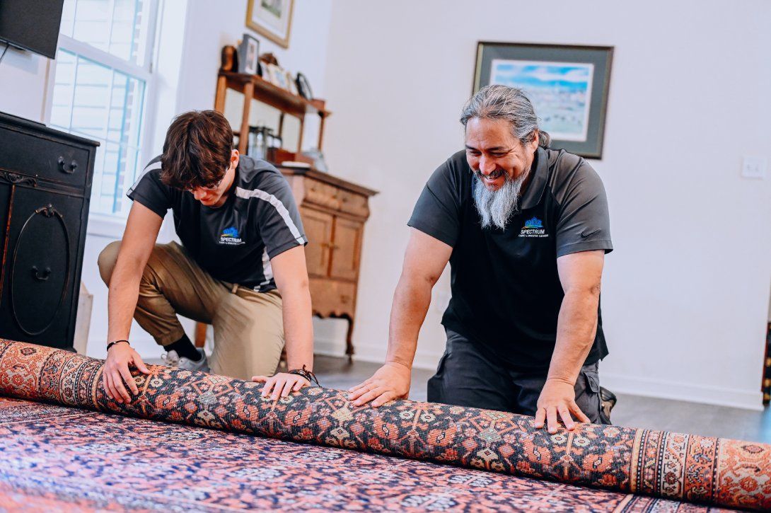 Two men rolling out a patterned rug in a light-filled room, smiling.