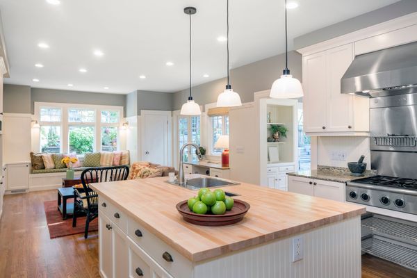 Cuisine lumineuse avec îlot en bois, appareils électroménagers en acier inoxydable et banquette près de la fenêtre offrant une vue.