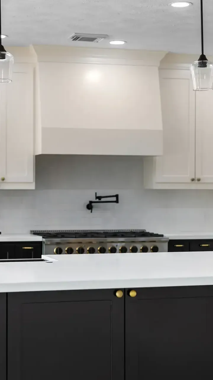 A kitchen with white cabinets , black cabinets , a stove and a sink.