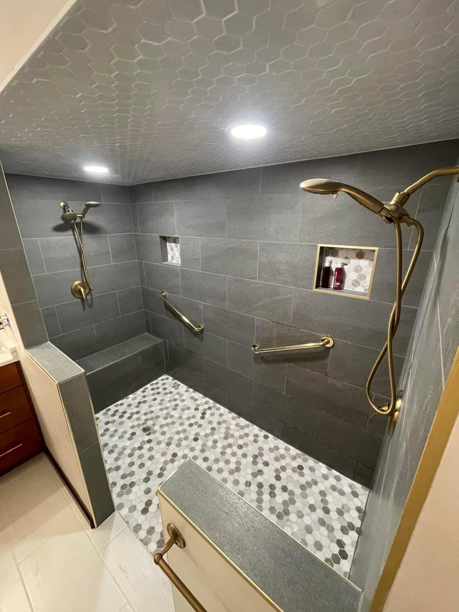 Custom walk-in shower with dual shower heads, built-in bench seating, grab bars, and hexagon tile design by A&J Remodel and Construction