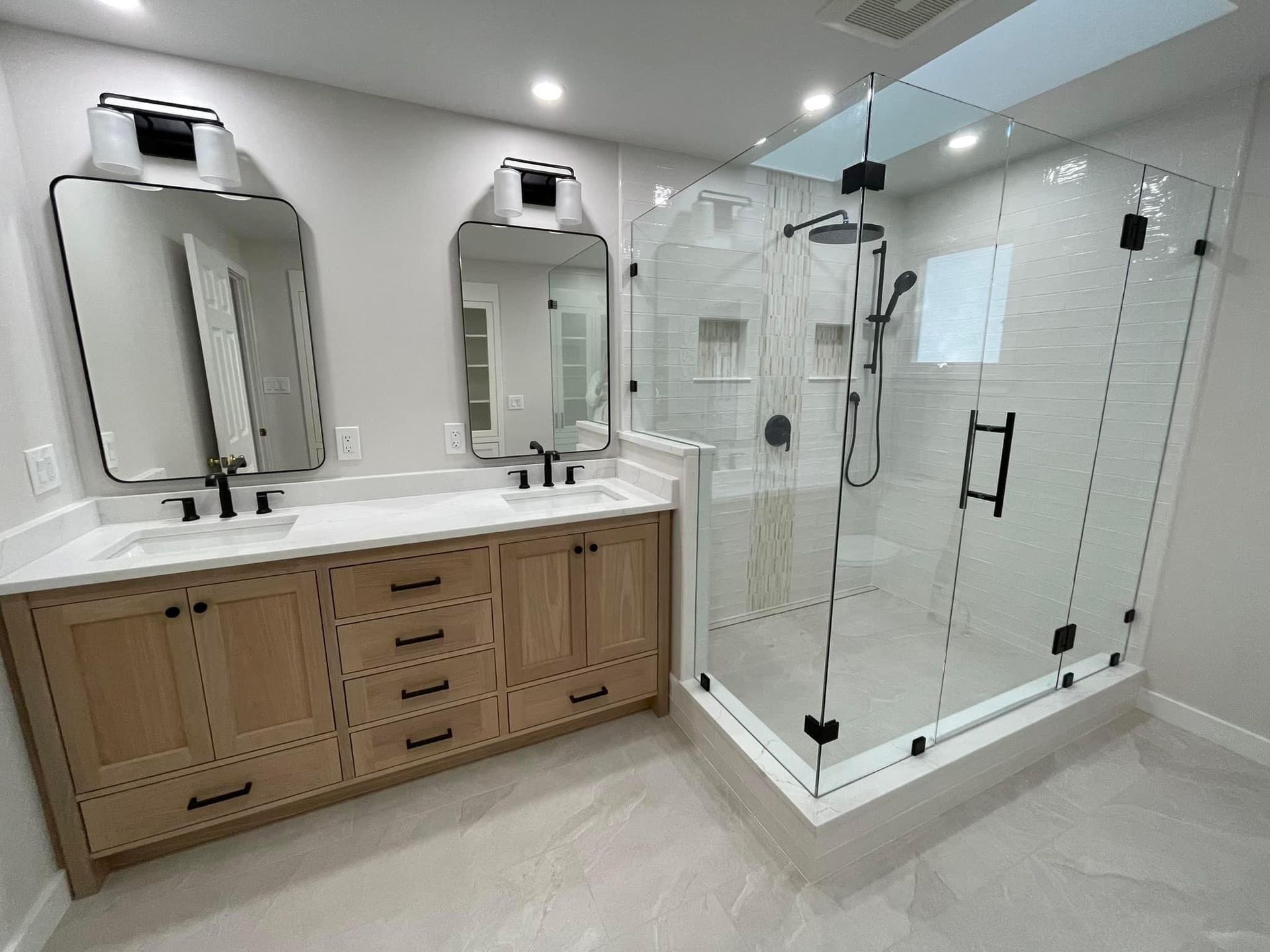 Contemporary bathroom with double vanity, wood cabinetry, frameless glass shower enclosure, and matte black fixtures by A&J Remodel and Construction