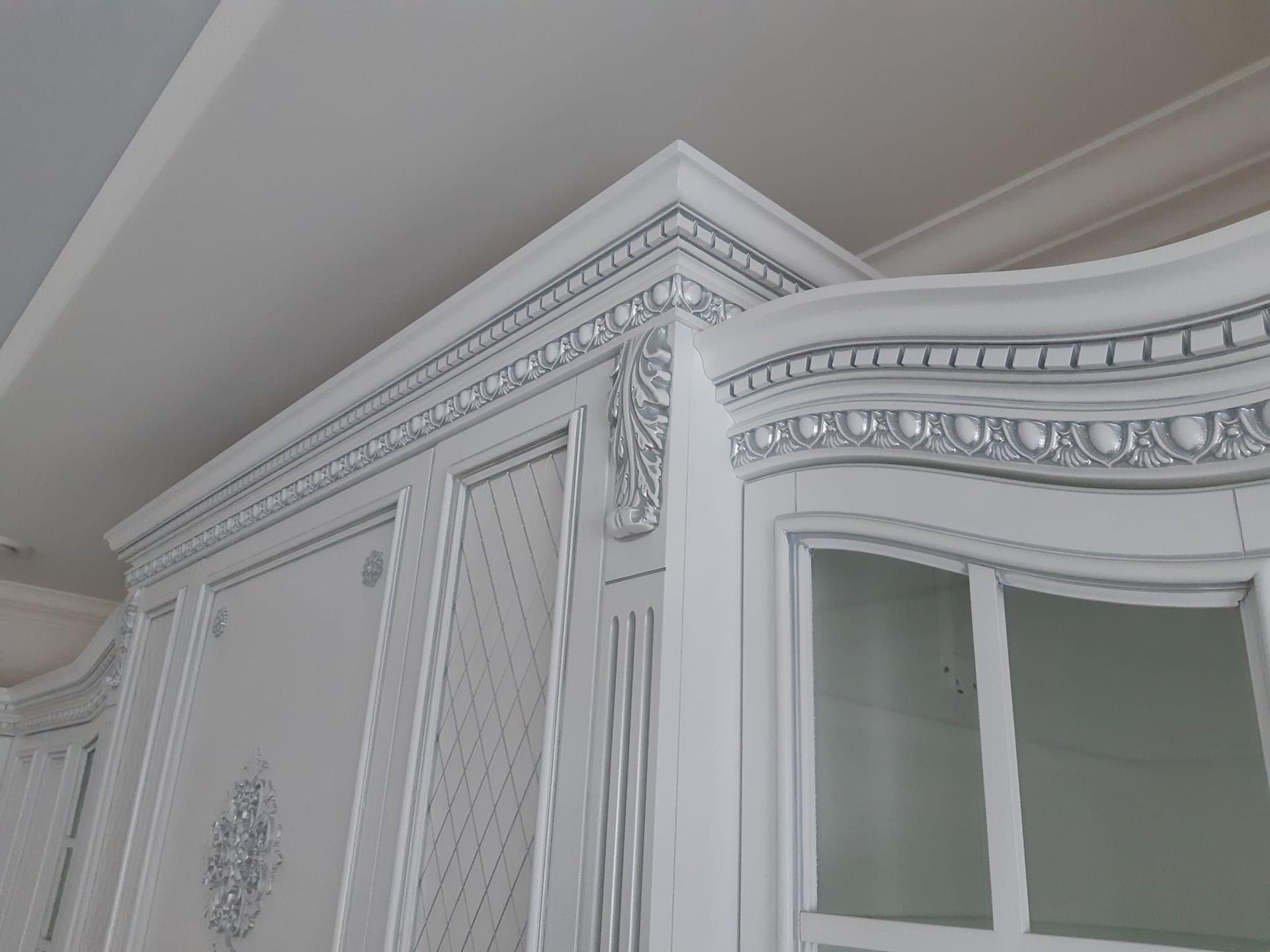 Elegant white cabinetry with intricate silver ornamental detailing and glass-paneled doors, crafted by A&J Remodel and Construction