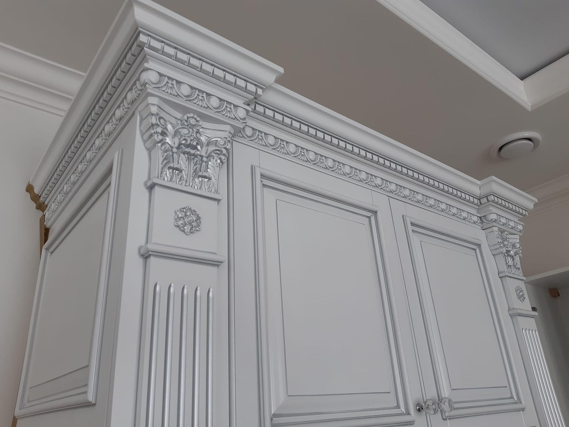 Close-up of ornate white cabinet with decorative crown molding, fluted columns, and intricate corbels by A&J Remodel and Construction