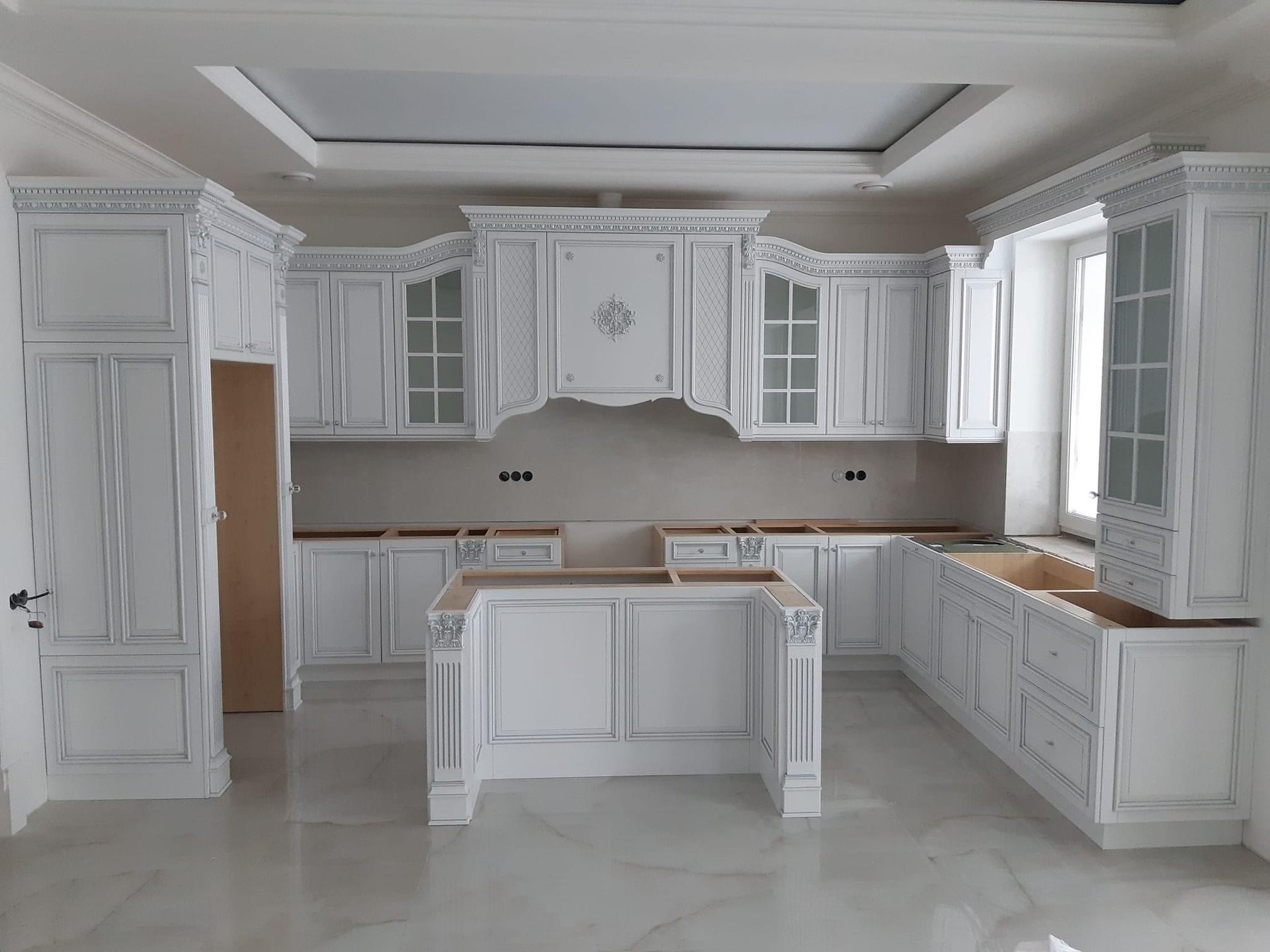 Spacious white luxury kitchen with detailed crown molding, glass-front cabinets, and custom island cabinetry by A&J Remodel and Construction