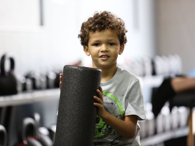 a young boy is holding a black foam roller in a gym .