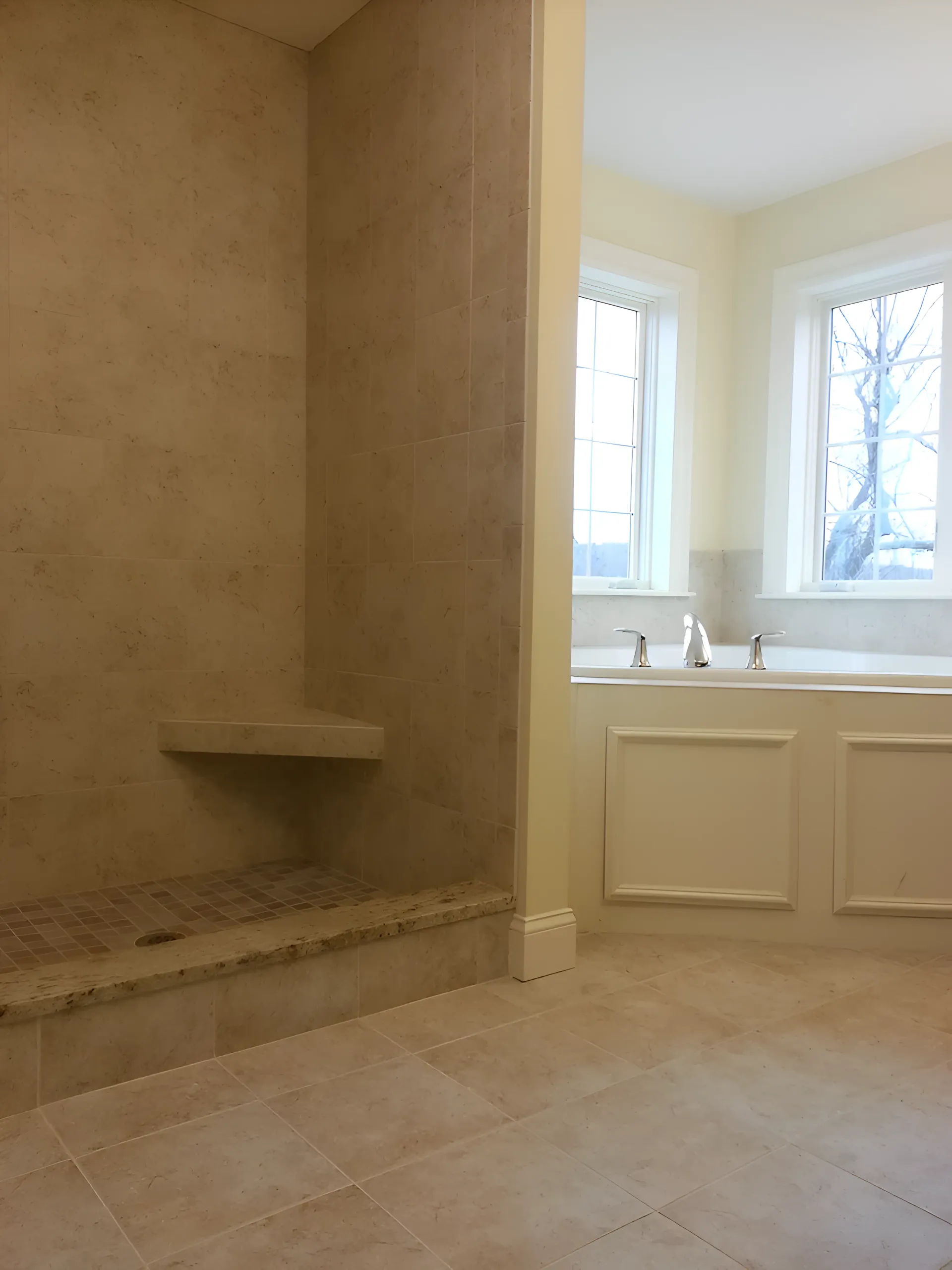 Bathroom with tiled shower and built-in bench, adjacent to a bathtub with windows.