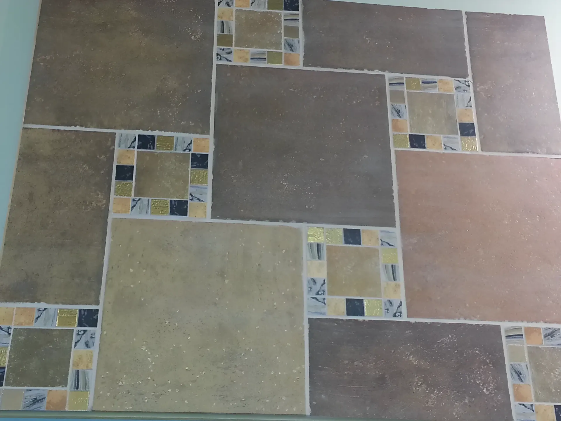 Tiled wall with large square and rectangular tiles in shades of brown, with decorative mosaic squares in between.