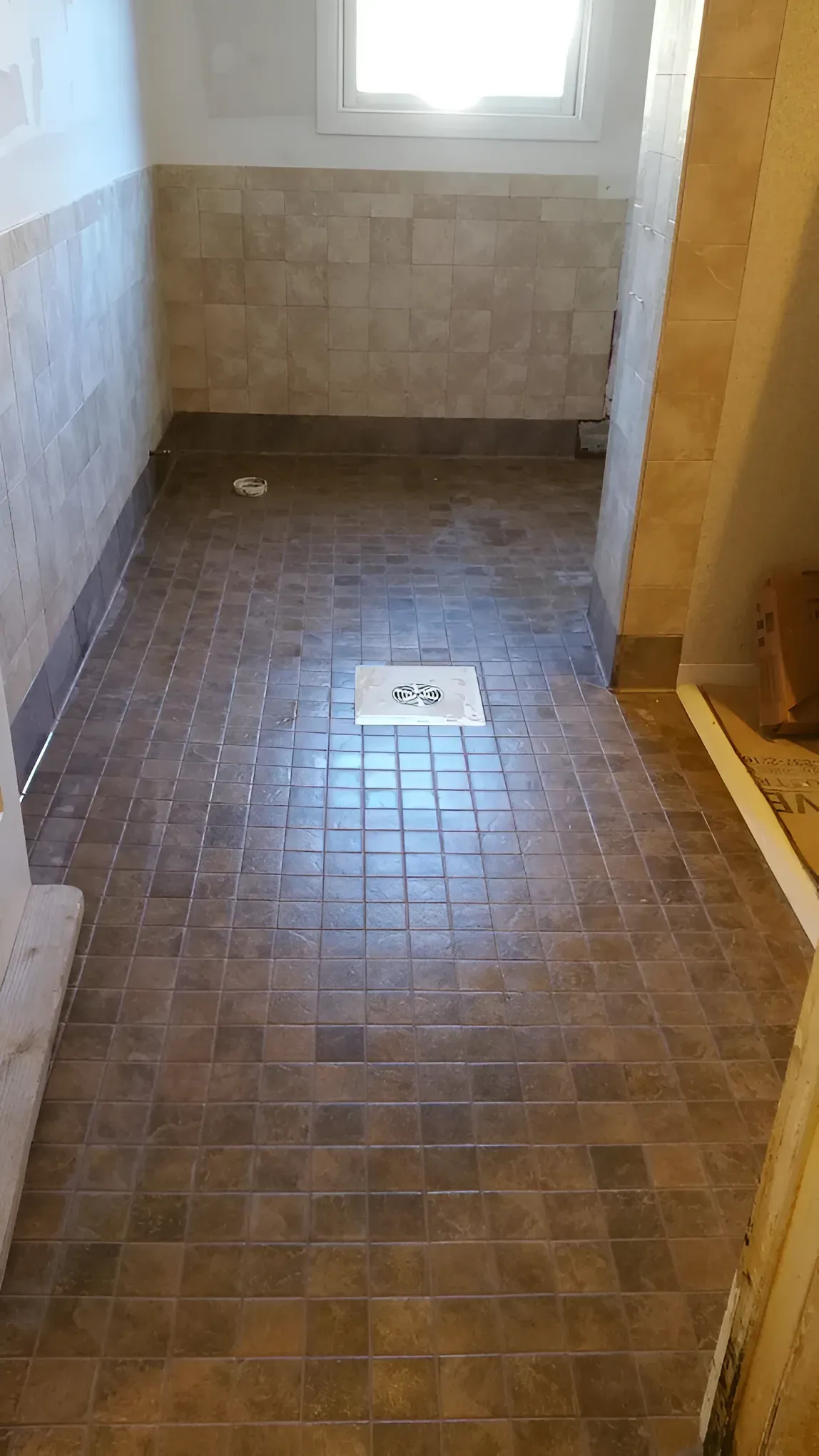 Bathroom with brown tile floor and walls, a window, and a drain in the center.