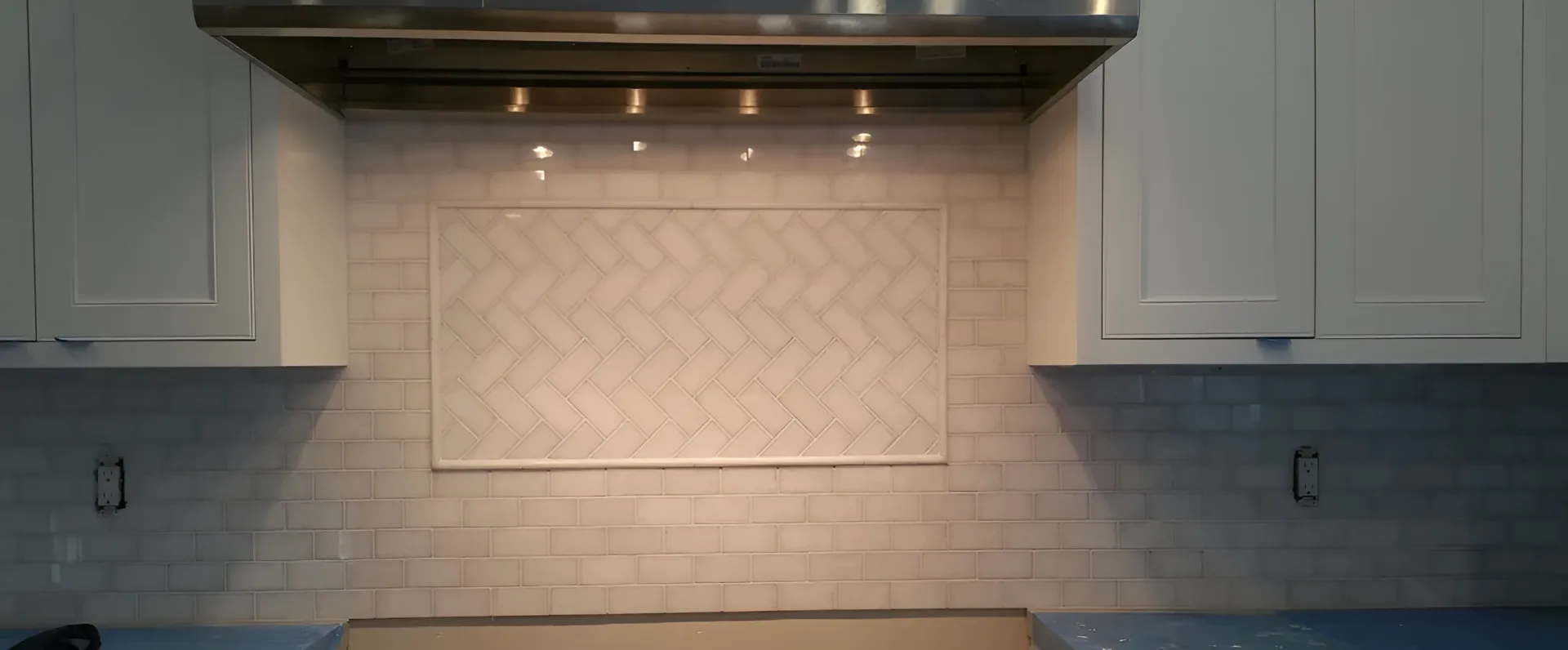 Kitchen backsplash with herringbone tile accent. White cabinets and range hood.