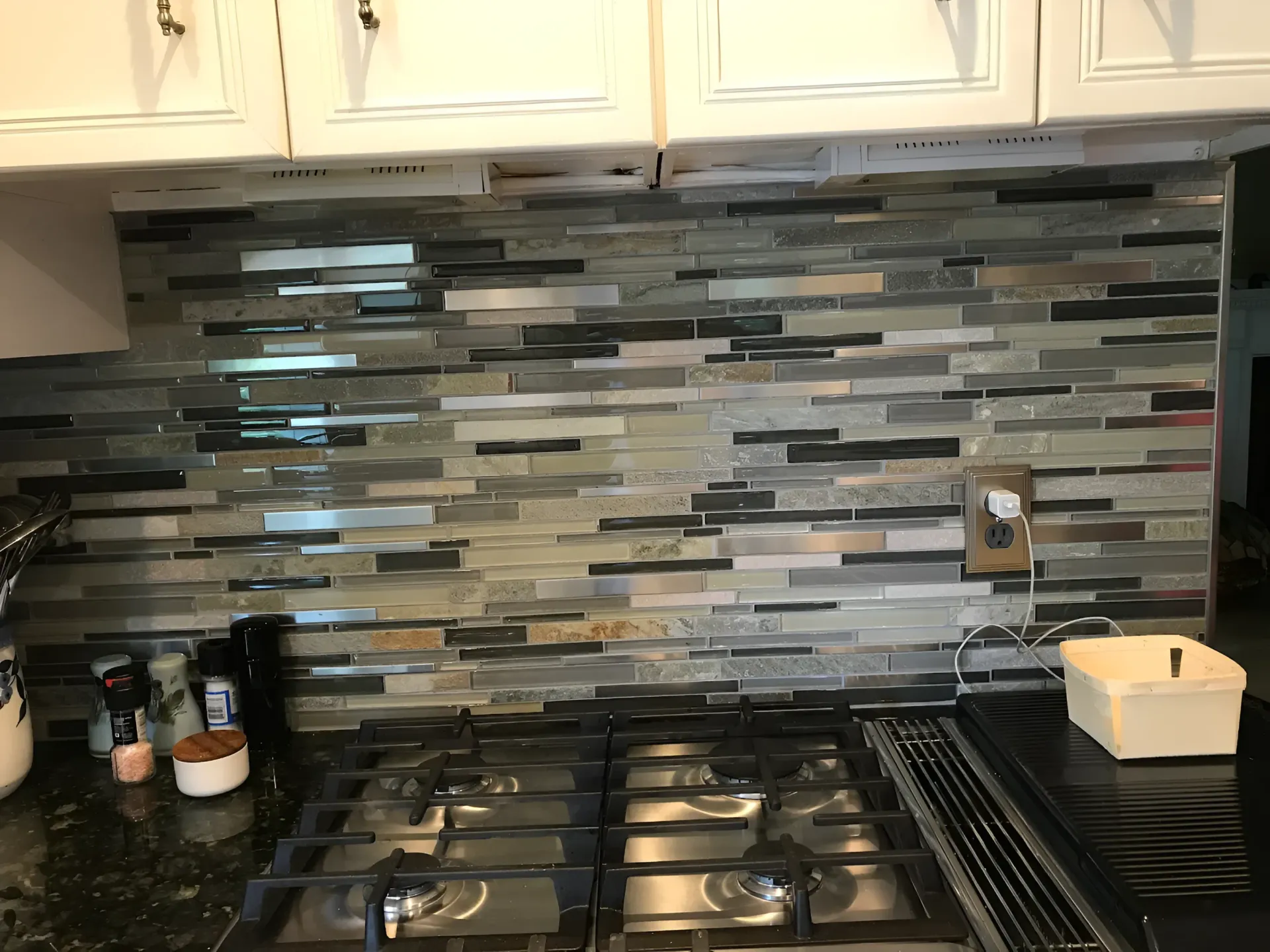 Kitchen backsplash with dark, mosaic-style tiles above a stovetop.