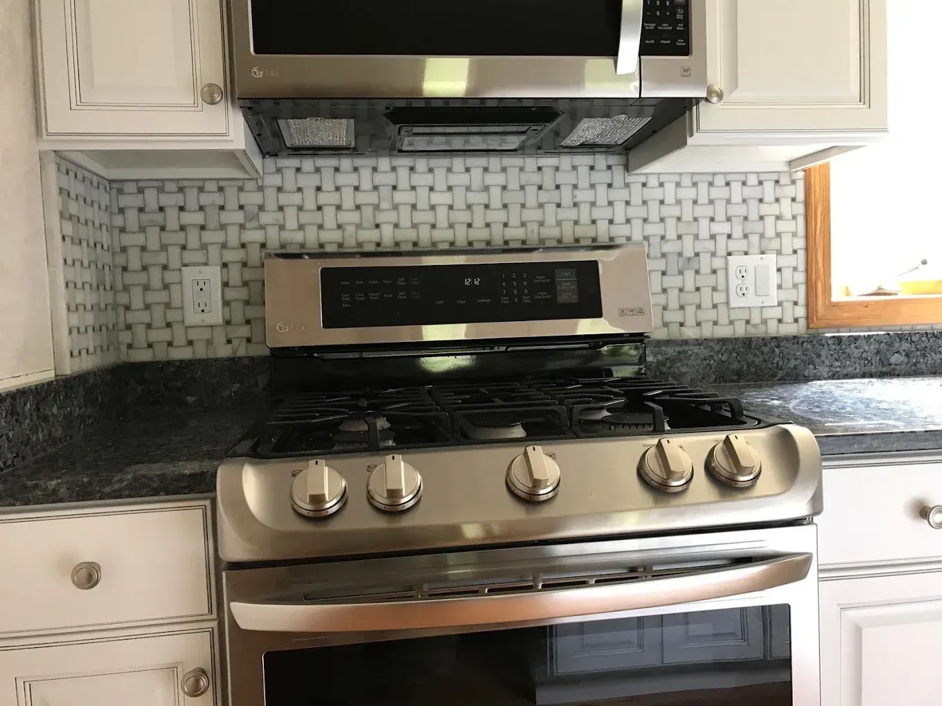 Stainless steel stove and microwave in a kitchen with white cabinets and patterned backsplash.