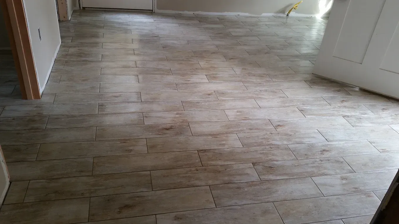 Tiled floor in a room with light brown rectangular tiles, doors and walls in sight.