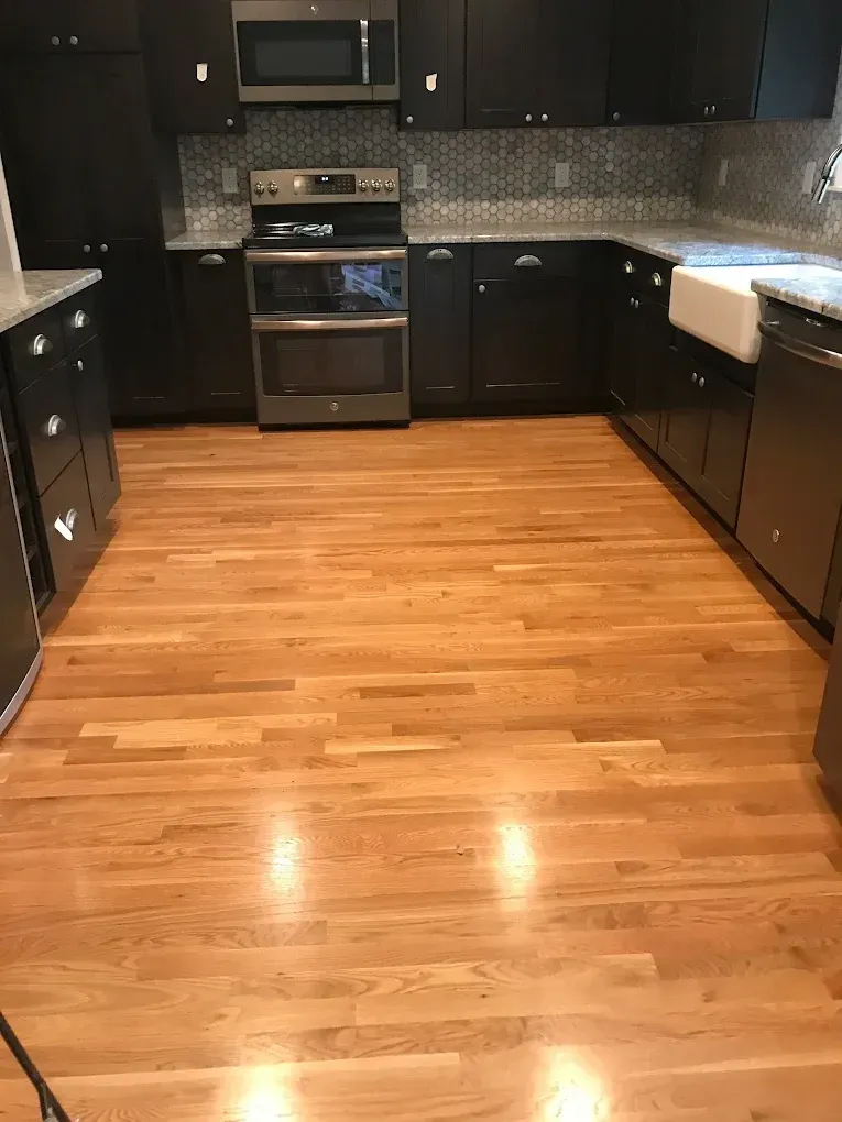 Kitchen with hardwood floors, dark cabinets, stainless steel appliances, and a white farmhouse sink.