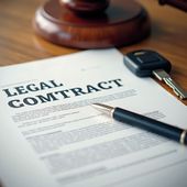 Legal contract with pen, car key, and gavel on a wooden table.