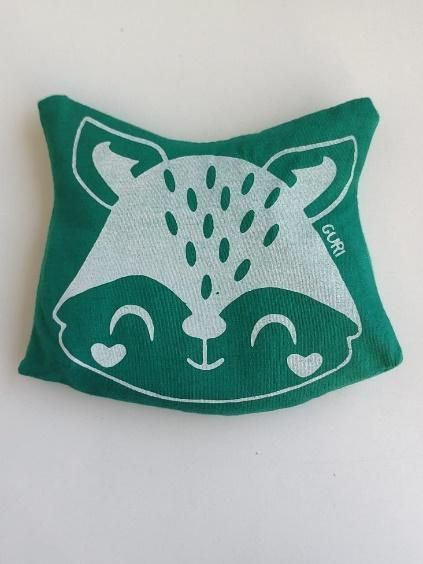Almohada verde con diseño de cara de mapache blanco sonriente.