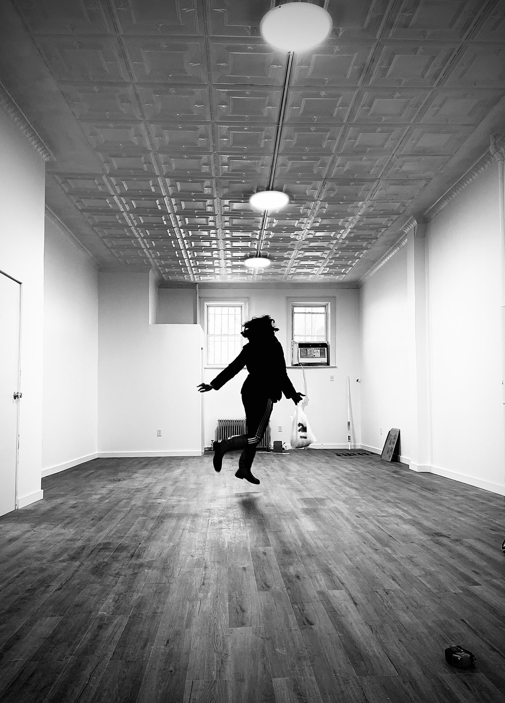 Person jumping in empty room with patterned ceiling and wooden floor.