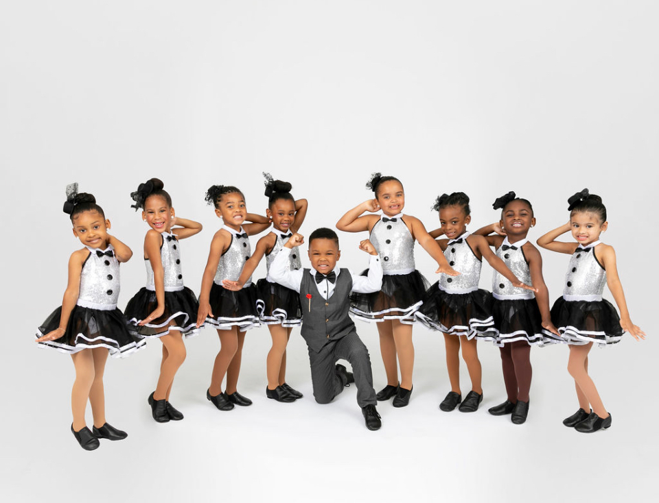 Group of kids in formal wear poses on white backdrop.