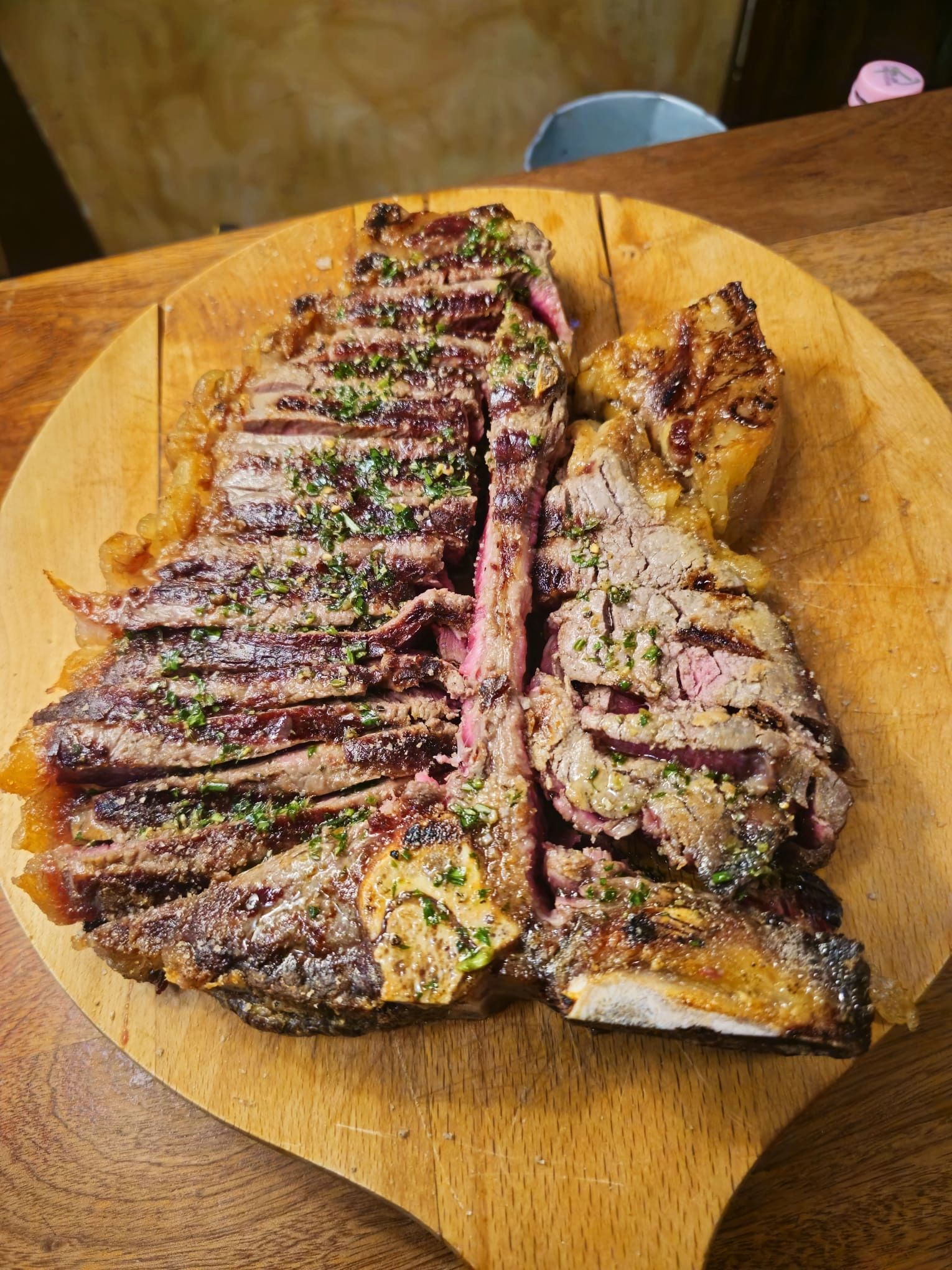 Bistecca di manzo alla griglia tagliata a fette su un tagliere di legno, condita con erbe aromatiche.
