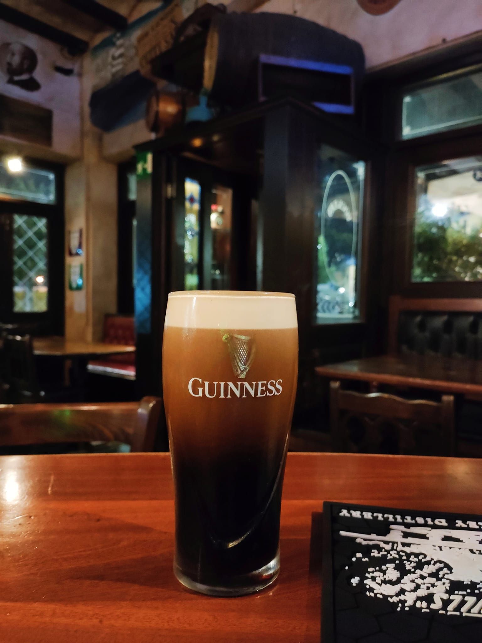 Una pinta di Guinness sul bancone di un pub irlandese; birra scura con schiuma cremosa.