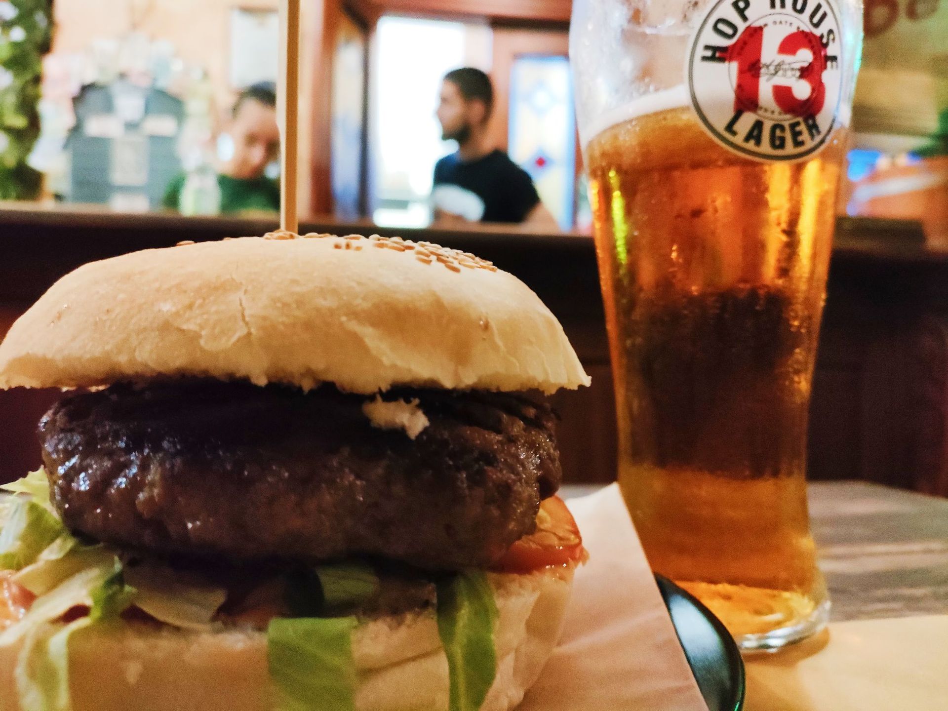 Hamburger con birra, su un tavolo in un bar. Persone sfocate sullo sfondo.