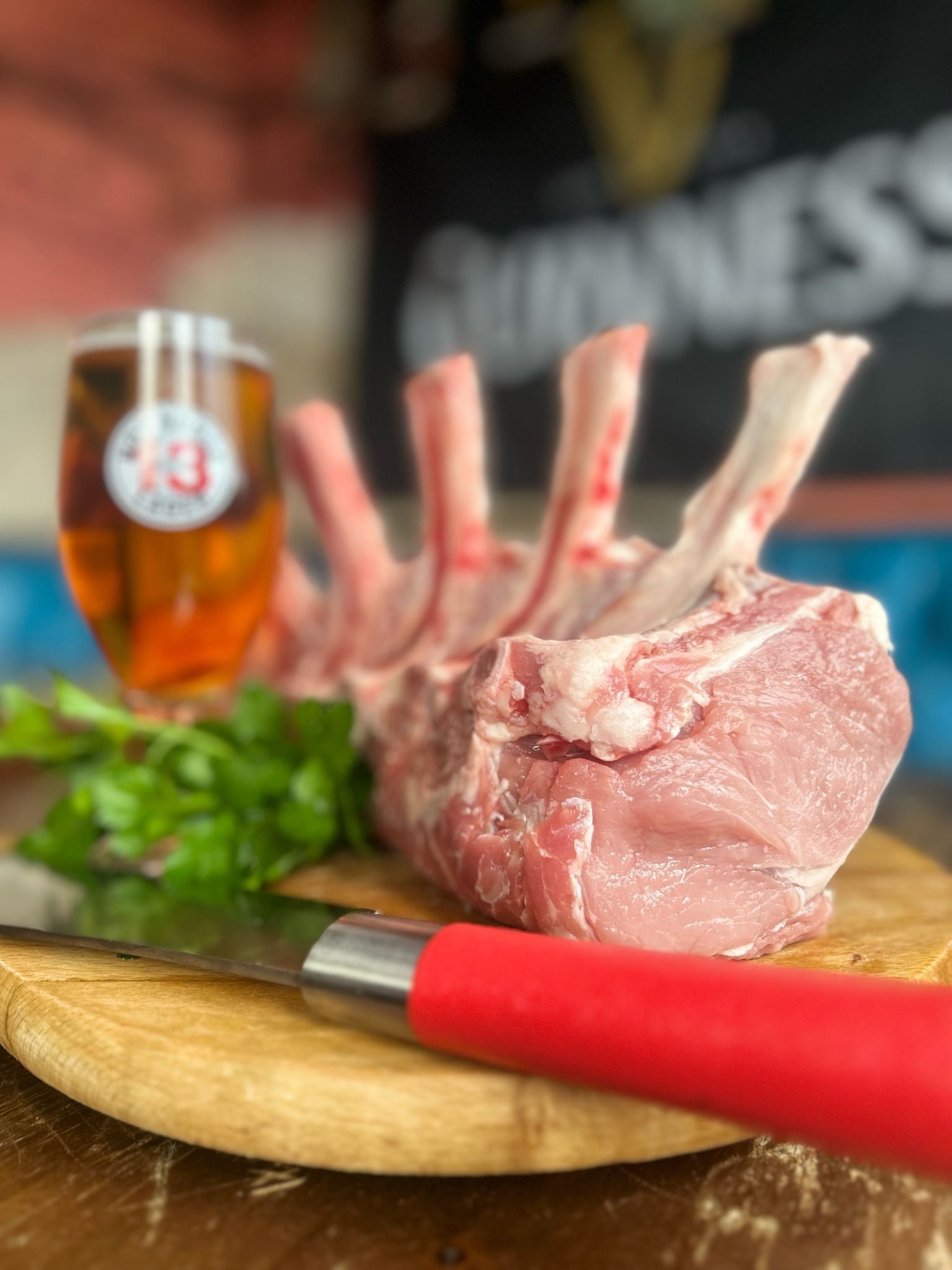 Arrosto di maiale a corona su un tagliere di legno con prezzemolo, coltello e birra.