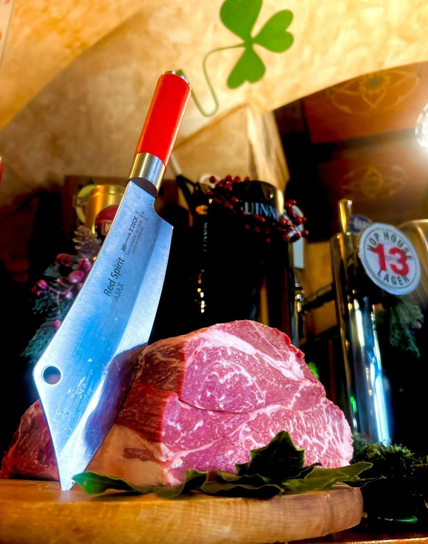 Coltello da macellaio infilzato in un pezzo di carne cruda su un tagliere di legno.