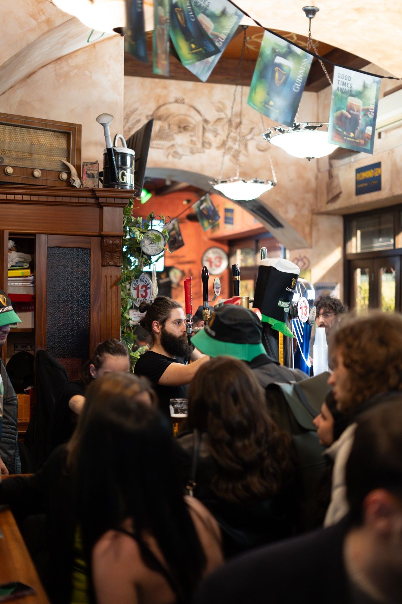 La gente si accalcava all'interno di un pub, alcuni con cappelli verdi, con poster e un soffitto decorato.
