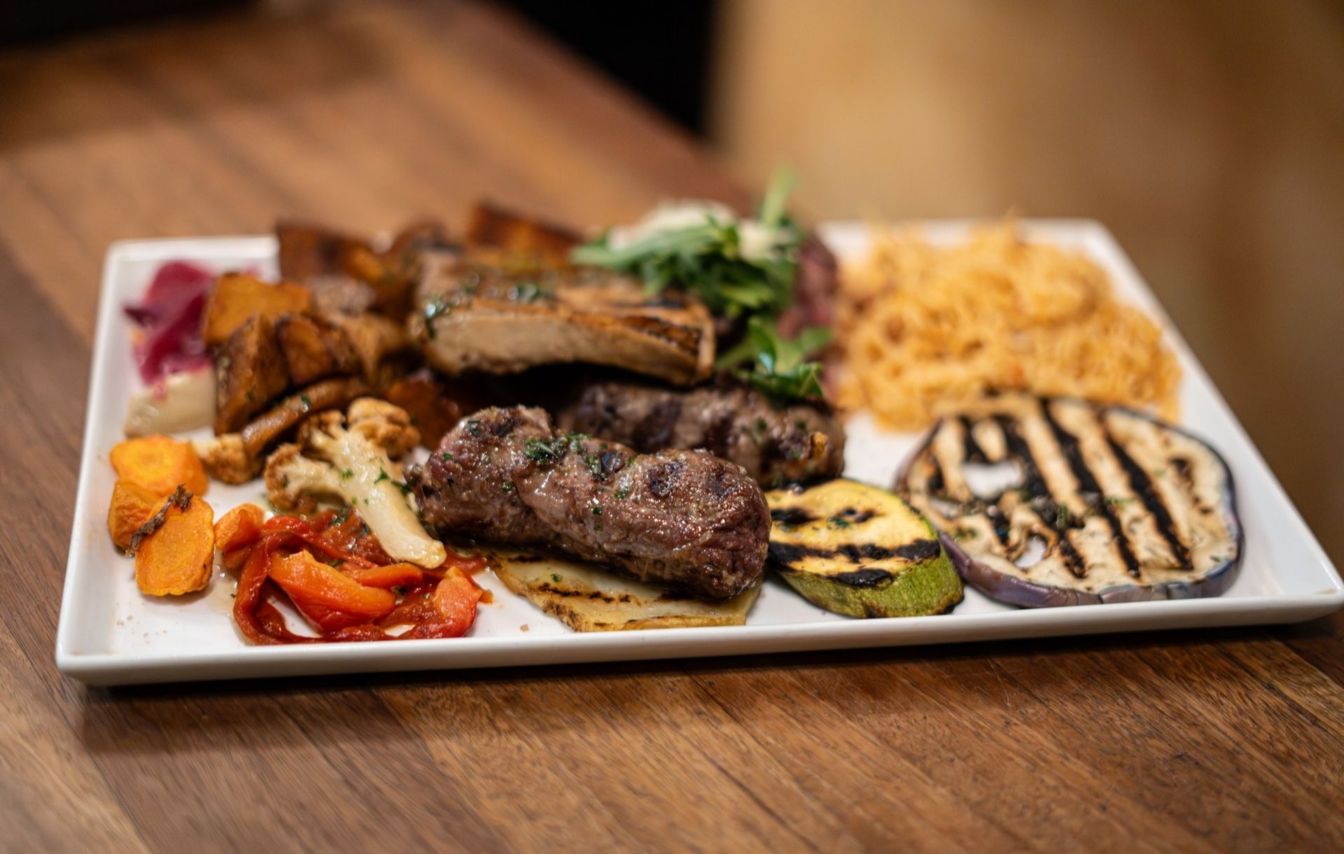 Carne e verdure alla griglia su un piatto bianco, tra cui melanzane, zucca e patate dolci.