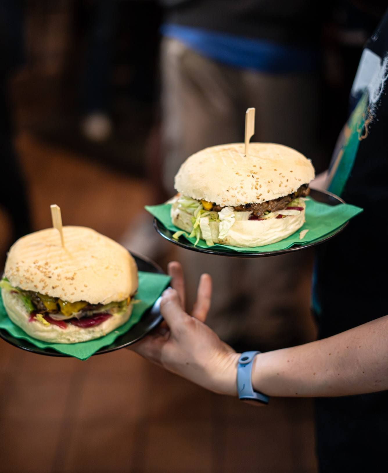 Due hamburger su piatti tenuti da una persona. Fa capolino un po' di lattuga verde.
