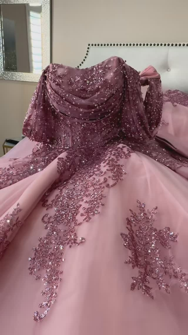 A pink ball gown is sitting on top of a bed.