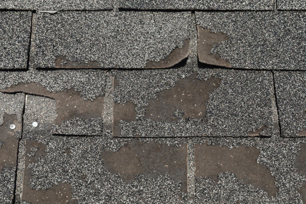 Damaged asphalt roof shingles; granular coating is peeling off, exposing the black underlayment.