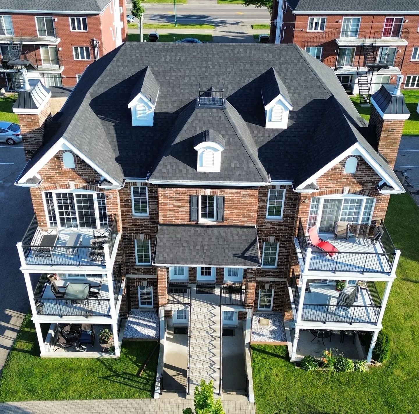 Multi-story brick building with balconies, dark roof, and landscaped lawn.