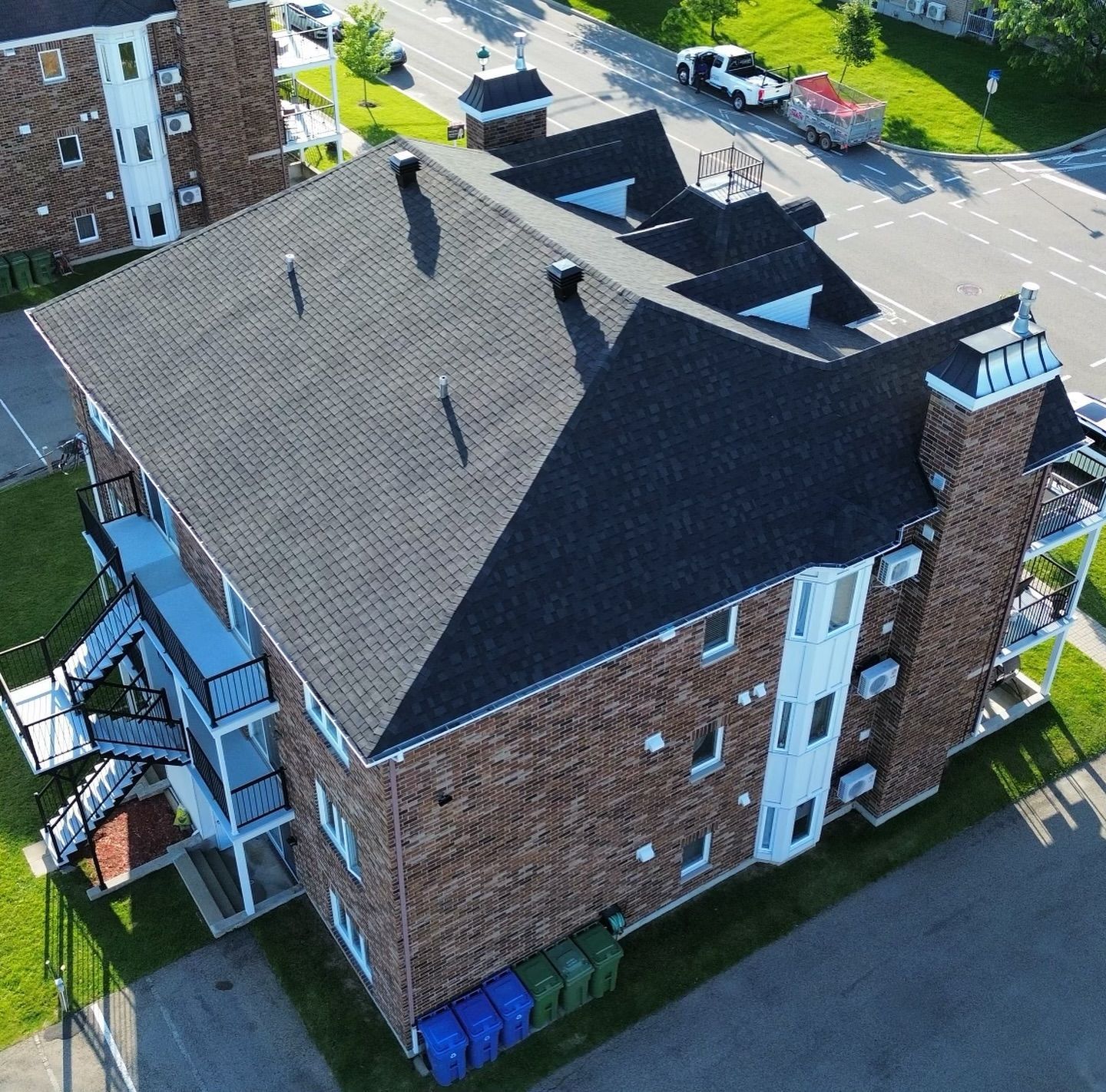 Vue aérienne d'un immeuble d'appartements en briques avec un toit sombre, des balcons et de l'herbe verte qui l'entoure.