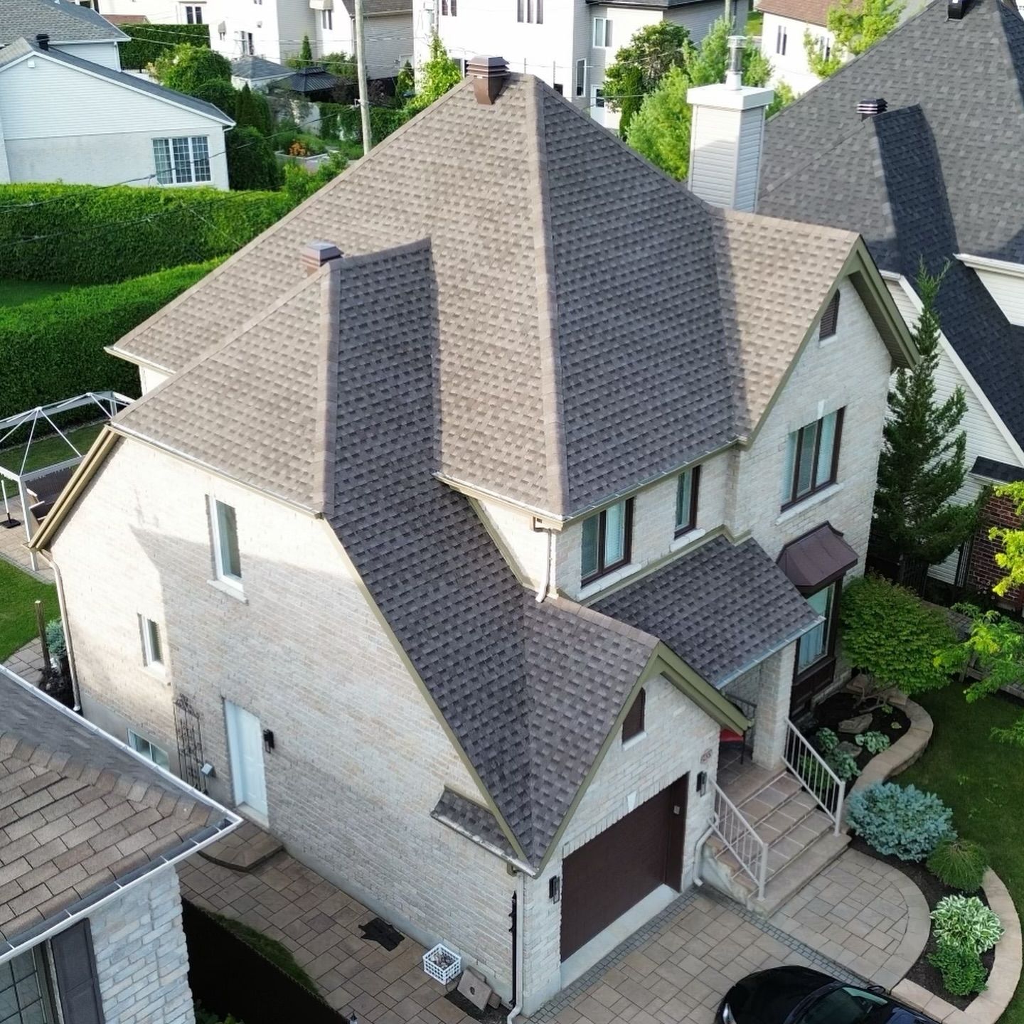 Maison de deux étages en briques beiges avec toit en bardeaux bruns et garage attenant. Située dans un quartier résidentiel verdoyant.