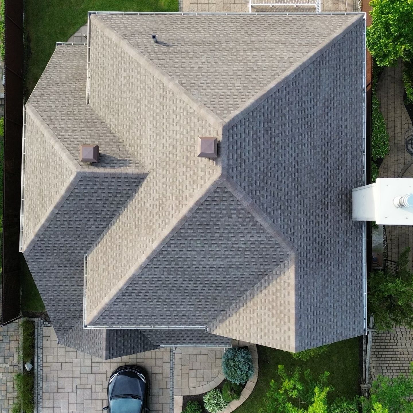 Vue aérienne d'une maison au toit de bardeaux gris à multiples facettes. Une voiture est garée dans l'allée.