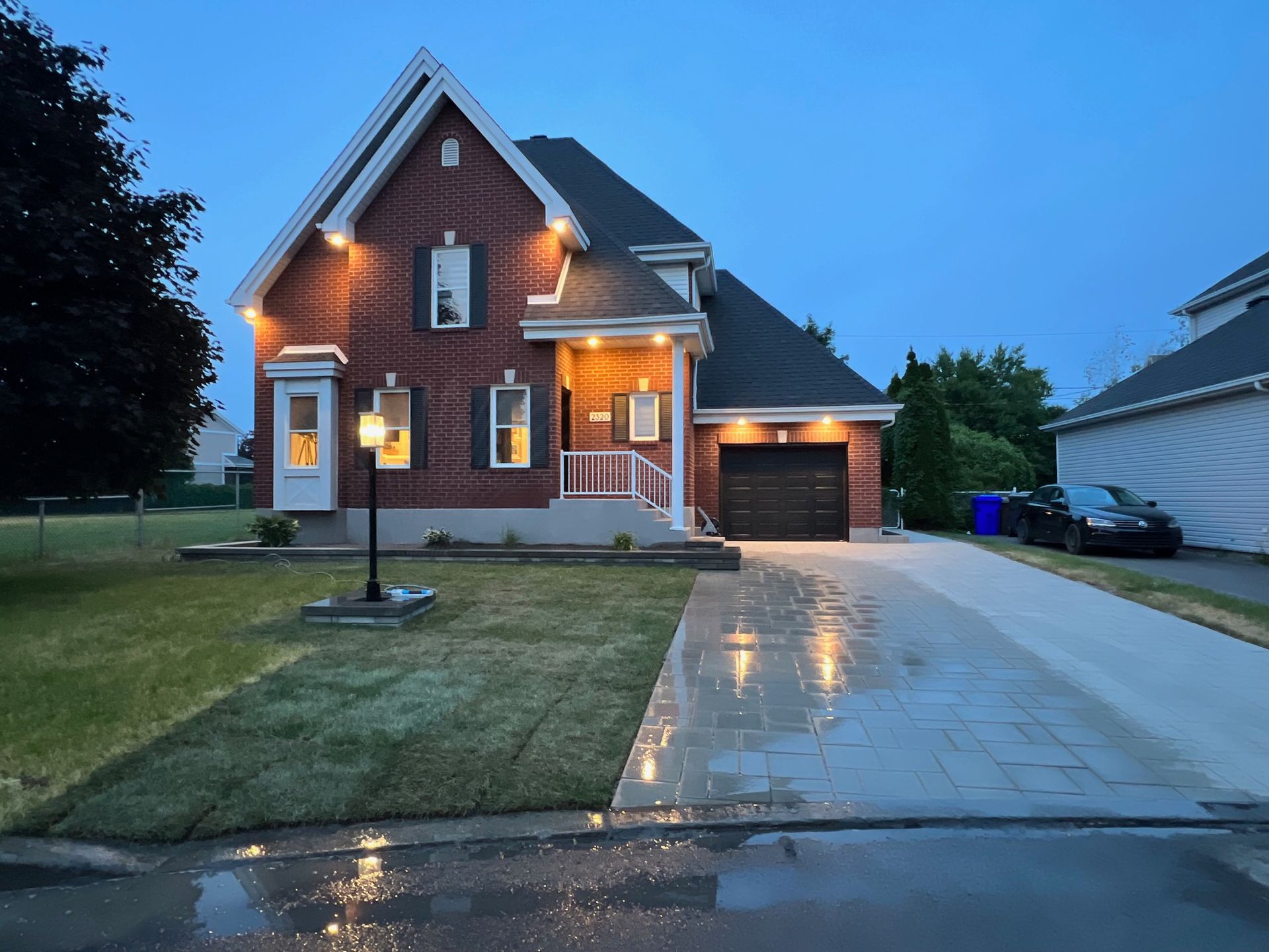 Une maison en briques est éclairée la nuit avec une voiture garée devant elle