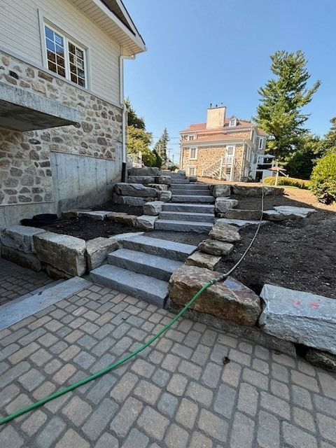 Un tuyau est posé sur un patio en briques à côté d'un escalier menant à une maison.