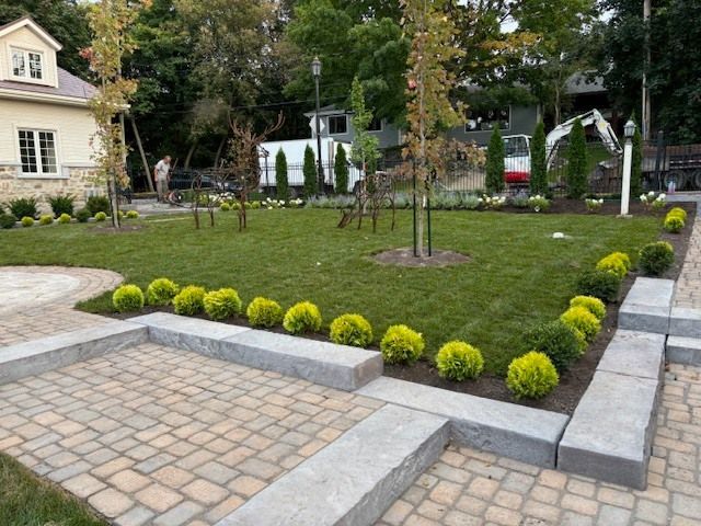 Une cour verdoyante avec une allée en briques et une maison en arrière-plan