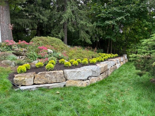 Un jardin verdoyant et luxuriant avec un mur de pierre entouré d'arbres et d'arbustes.